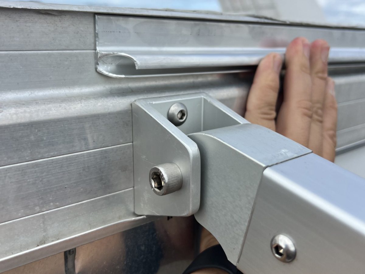 Close-up of a machined DMP bracket joining the aluminum awning frame to the rail on a trailer wall