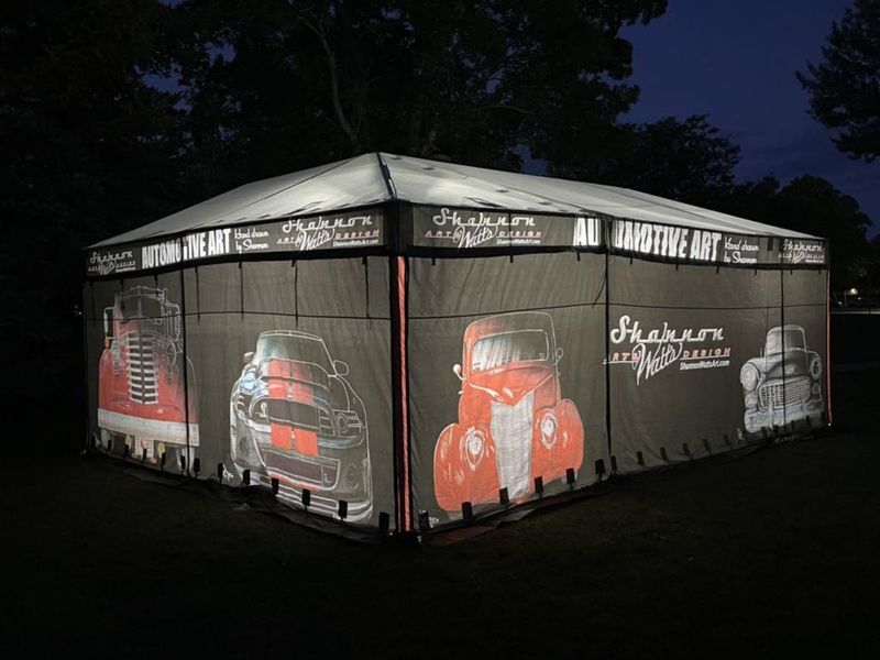 Shannon Watts Art sales enclosure lit from inside at night, its walls printed with classic car art